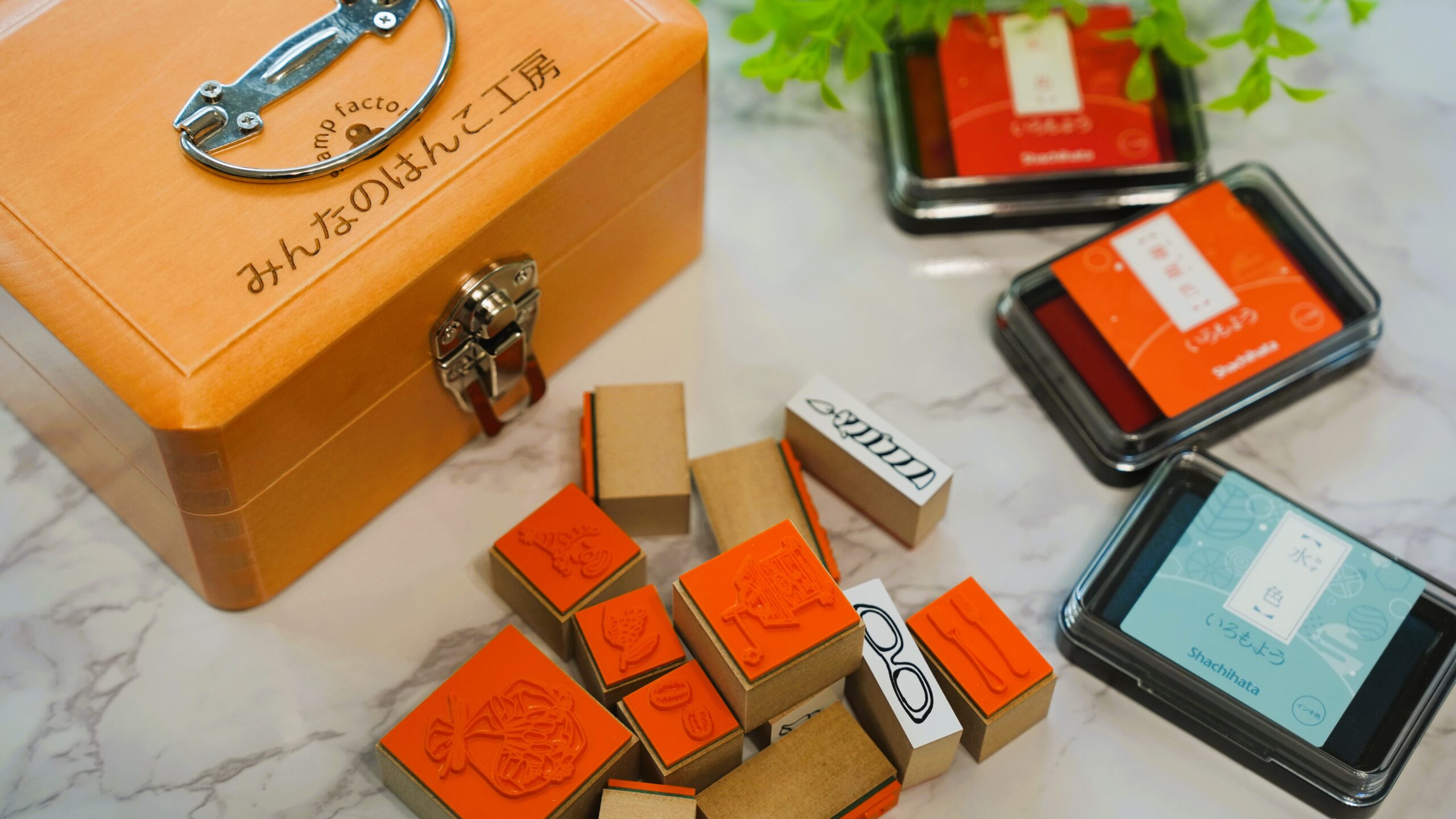 色とりどりのインクパッドとはんこを並べた作業スペース。スタンプ作品が並ぶ温かい雰囲気の写真。