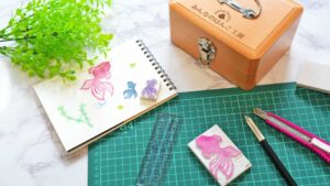 木の机の上に並んだ手彫りのはんこ、スケッチブック。はんこ作家の制作風景をイメージした写真。