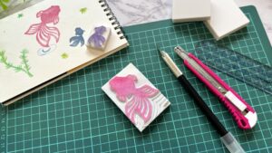 はんこ作家を目指す人のために、彫刻刀と手彫りはんこ、スケッチが並ぶ制作風景を写した写真。