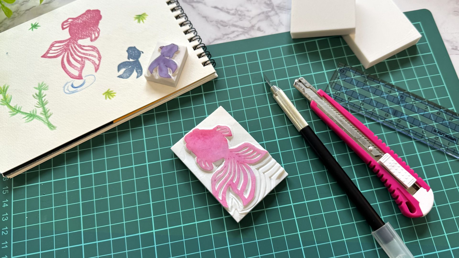 はんこ作家を目指す人のために、彫刻刀と手彫りはんこ、スケッチが並ぶ制作風景を写した写真。