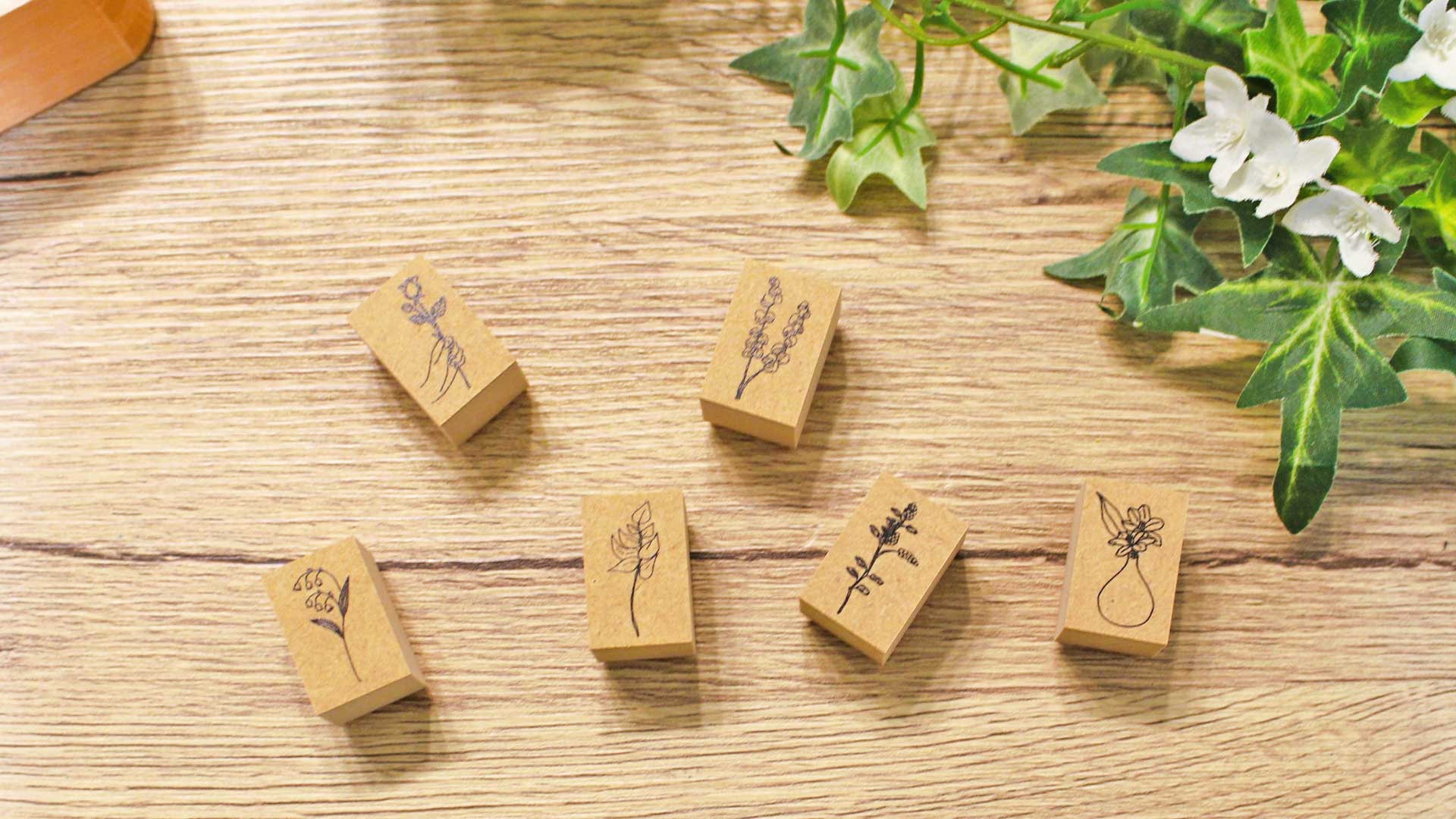 手帳の上に花や動物のオリジナルスタンプが並び、優しい光に包まれた癒しを感じる文具コーナーのイメージ。