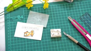 作業机の上に並ぶはんこ用イラスト素材や彫刻道具、完成したスタンプ作品の写真