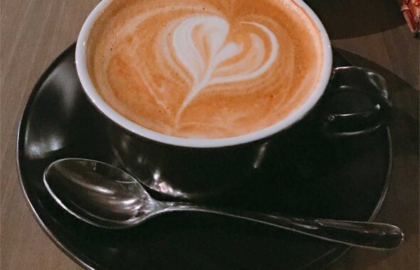 木のテーブルの上にコーヒーカップの中にコーヒーが入っていて、クリームでハートマークになっているほっこりした画像