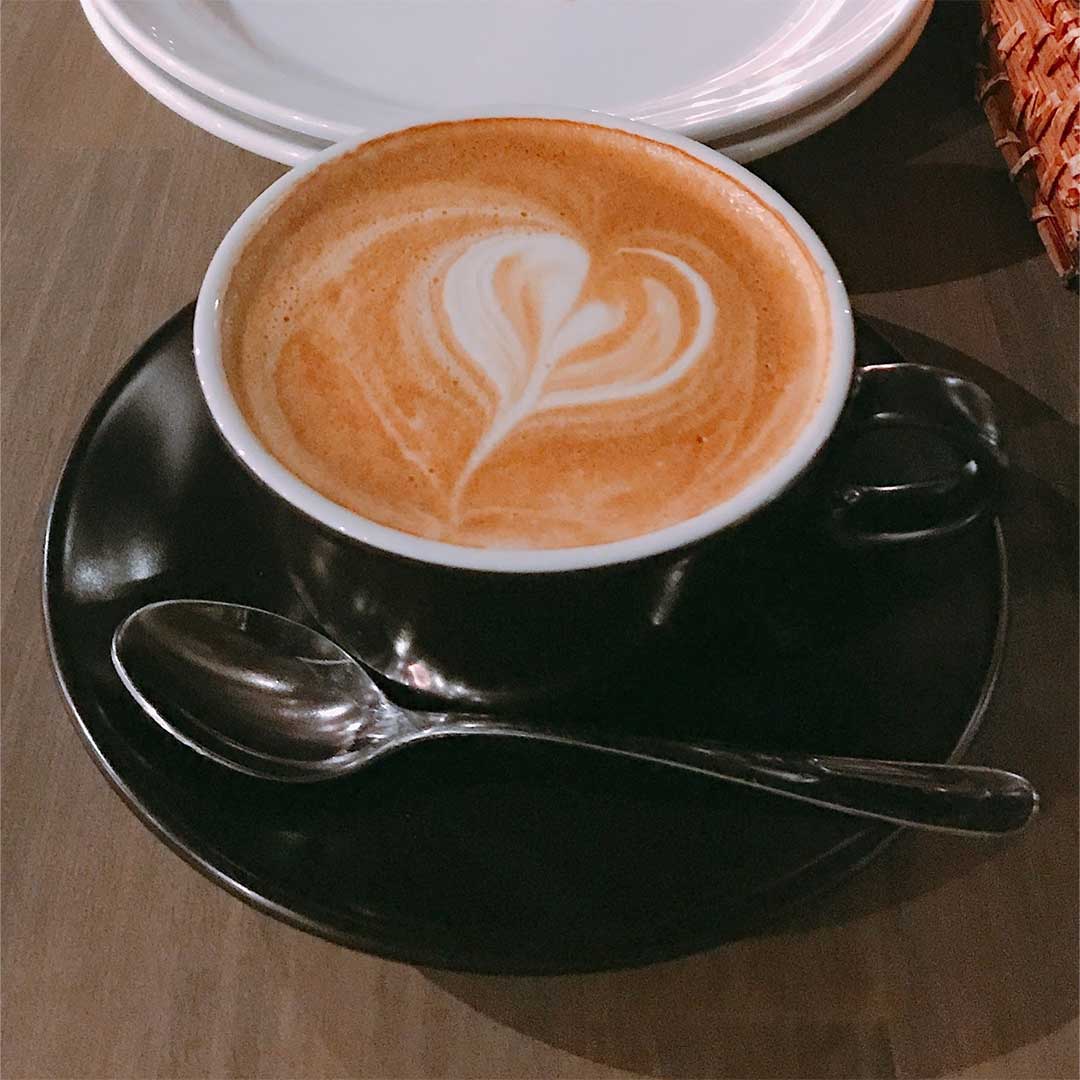 木のテーブルの上にコーヒーカップの中にコーヒーが入っていて、クリームでハートマークになっているほっこりした画像